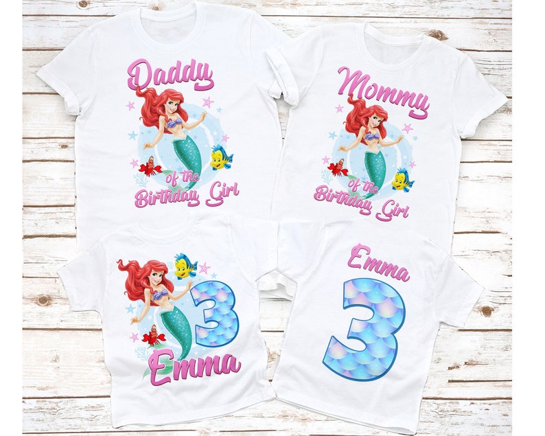 May include: Set of four white t-shirts with a mermaid theme. The shirts feature a pink and white design with the words "Daddy of the Birthday Girl", "Mommy of the Birthday Girl", "Emma" and a number "3" with a mermaid tail design.