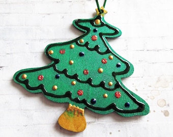 May include: A green wooden Christmas tree ornament with a gold star on top. The tree is decorated with gold, red, and blue dots.