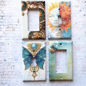 May include: Four decorative light switch covers with different designs. The top left cover features a gold and blue design with a clock face and stars. The top right cover features a sun and moon design with gold and blue accents. The bottom left cover features a blue butterfly with gold accents. The bottom right cover features a blue and green watercolor design with gold stars.