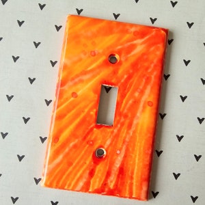 Op de afbeelding: Een oranje en witte lichtschakelaar met een marmerpatroon.