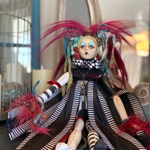 May include: A whimsical doll with a black and white striped dress, red hair, and a crown. The doll has a painted face with blue eyes and a black and white checkered collar.