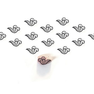 May include: A collection of small, black cloud-shaped stamps arranged in a diamond pattern on a white background. A single stamp with a pink cloud design is also visible. The stamps are likely used for crafting or scrapbooking.