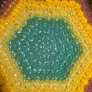 Peut inclure: Une couverture au crochet avec un motif ombré arc-en-ciel. La couverture est faite de fils de différentes nuances de brun, jaune, vert et bleu. Le centre de la couverture est de couleur bleu unie.