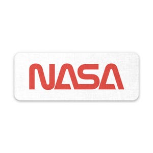 Op de afbeelding: Een witte rechthoekige sticker met het woord "NASA" in rode letters.