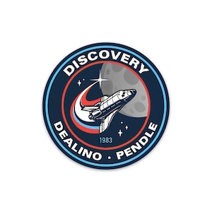 May include: A blue and white circular sticker with the text "DISCOVERY DEALINO PENDLE 1983" around the edge. The center of the sticker features a space shuttle flying past a crescent moon with stars in the background.