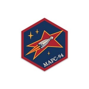 May include: A red and blue hexagonal patch with a white rocket ship flying through a red star. The star has a yellow outline and there are three yellow stars in the background. The text "MAPC-94" is printed in white at the bottom of the patch.