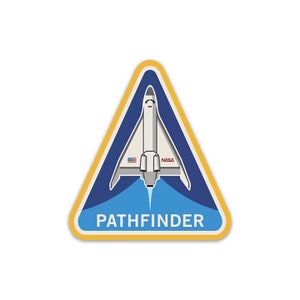 Puede incluir: Un parche triangular amarillo con fondo azul y una lanzadera espacial blanca con la palabra "PATHFINDER" en texto blanco. La lanzadera espacial tiene la bandera estadounidense y la palabra "NASA" en ella.