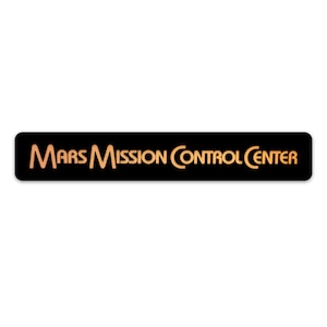 May include: Black rectangular sign with the text "MARS MISSION CONTROL CENTER" in gold lettering.