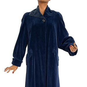May include: A long, navy blue velvet coat with a dark blue collar and a single button closure. The coat has long sleeves and two pockets. The coat is displayed on a mannequin.