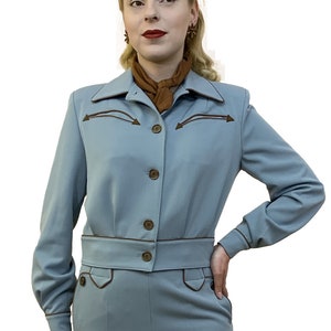 May include: A light blue trouser suit with brown trim. The jacket has a pointed collar and a button fastening. The trousers have a wide leg and belt loops.