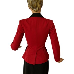 Puede incluir: Una chaqueta roja con cuello negro y falda negra. La chaqueta tiene una cintura ajustada y un dobladillo ligeramente acampanado.