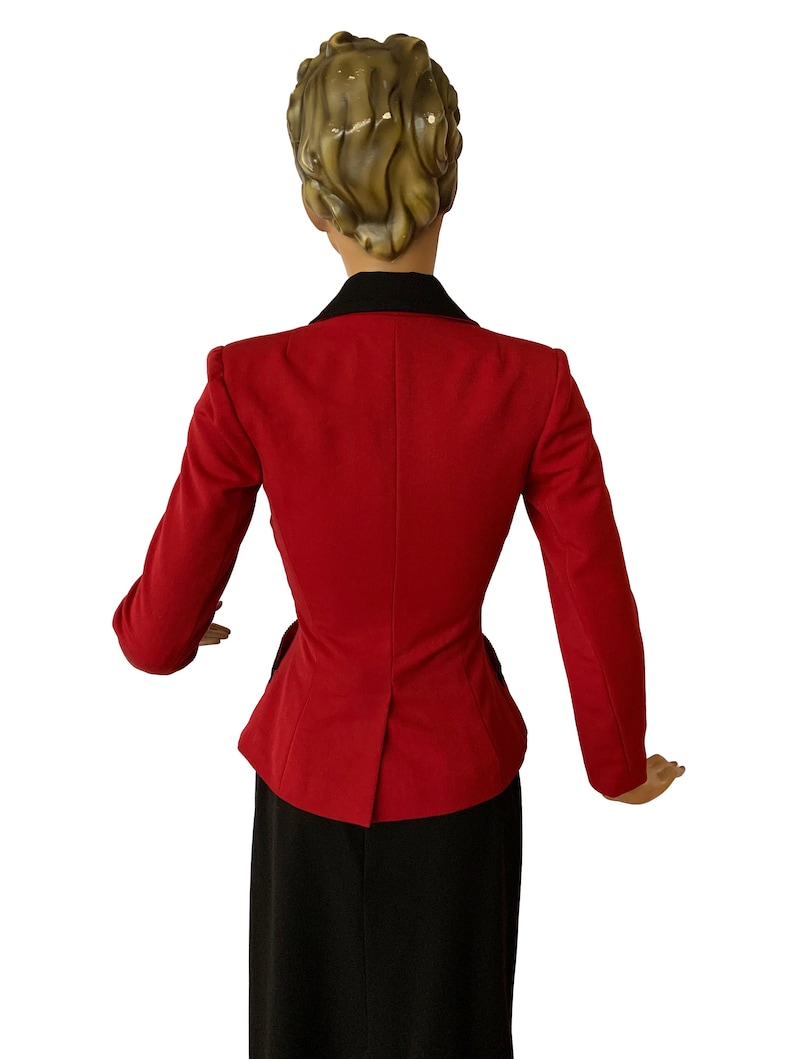 Puede incluir: Una chaqueta roja con cuello negro y falda negra. La chaqueta tiene una cintura ajustada y un dobladillo ligeramente acampanado.