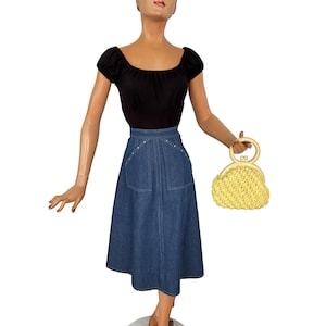 May include: A vintage outfit on a mannequin, featuring a black off-the-shoulder top and a denim skirt with pocket details. A yellow woven handbag with a circular handle completes the ensemble. The skirt falls to mid-calf length.