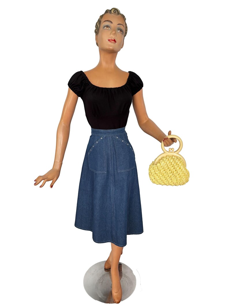 May include: A vintage outfit on a mannequin, featuring a black off-the-shoulder top and a denim skirt with pocket details. A yellow woven handbag with a circular handle completes the ensemble. The skirt falls to mid-calf length.