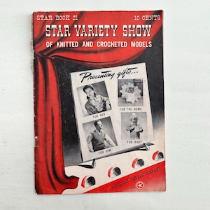 Op de afbeelding: Een vintage Star Book 21 patroonboekje getiteld Star Variety Show of Knitted and Crocheted Models. De rode omslag bevat een afbeelding van een podiumgordijn, zwart-witfoto's van gebreide modellen en de tekst Presenting gifts for her, him, home, and baby.