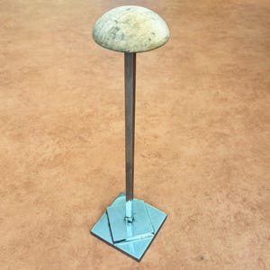 May include: A hat stand with a light-coloured, rounded top and a square base. The stand is made of metal and has a simple, minimalist design. The base is a square shape with a light blue colour.