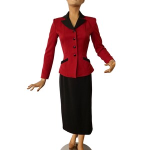 Puede incluir: Una chaqueta roja con cuello negro y botones negros, combinada con una falda negra. La chaqueta tiene una silueta ajustada y la falda es de largo hasta la rodilla.