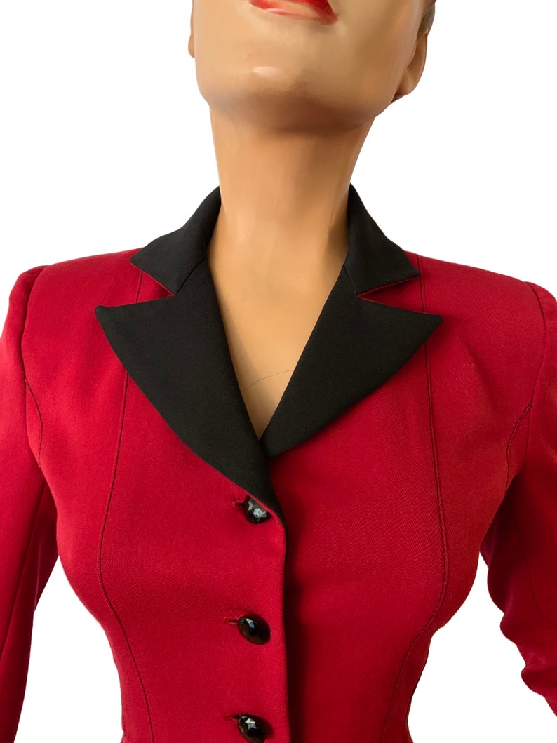 Puede incluir: Una chaqueta roja con cuello negro y cuatro botones negros. La chaqueta est&aacute; entallada y tiene una silueta ajustada.