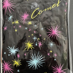 May include: Black plastic bag decorated with pink, yellow, and blue starbursts. The word "Comet" is written in yellow script. A white label at the bottom left reads "MAILLE FANTAISIE".