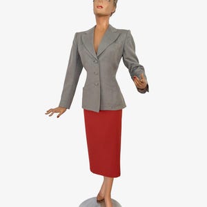 Puede incluir: Maniqu&iacute; con blazer gris y falda l&aacute;piz roja. El blazer tiene tres botones y dos bolsillos. La falda es hasta la rodilla. El maniqu&iacute; est&aacute; sobre una base plateada.