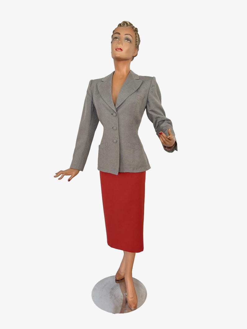 Puede incluir: Maniqu&iacute; con blazer gris y falda l&aacute;piz roja. El blazer tiene tres botones y dos bolsillos. La falda es hasta la rodilla. El maniqu&iacute; est&aacute; sobre una base plateada.