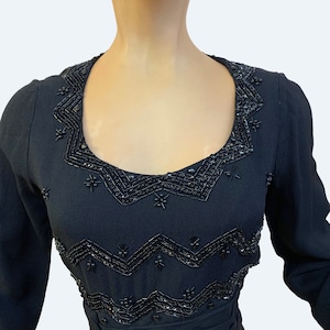 May include: A black dress with a beaded neckline. The beads are arranged in a geometric pattern.