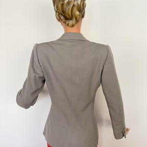 Puede incluir: Un blazer gris con un corte a medida, con mangas largas y un dise&ntilde;o cl&aacute;sico. El blazer se combina con una falda roja, creando una combinaci&oacute;n de colores contrastantes. La vista trasera muestra la estructura y el estilo de la prenda.