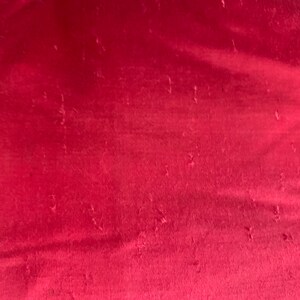 K&ouml;nnte beinhalten: Nahaufnahme eines tief roten Stoffes mit leicht strukturierter Oberfl&auml;che. Der Stoff hat einen dezenten Glanz und scheint aus einem weichen Material zu sein.