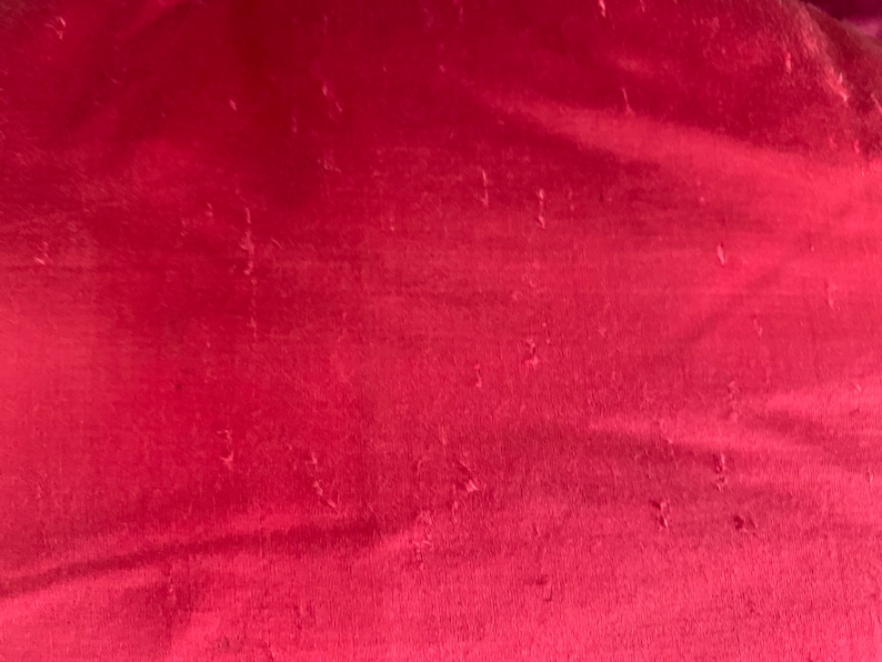 K&ouml;nnte beinhalten: Nahaufnahme eines tief roten Stoffes mit leicht strukturierter Oberfl&auml;che. Der Stoff hat einen dezenten Glanz und scheint aus einem weichen Material zu sein.
