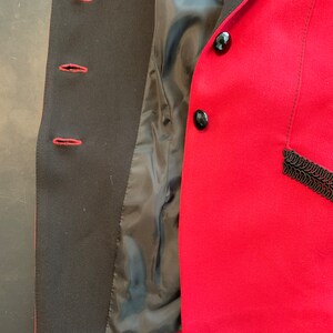 Puede incluir: Una chaqueta roja con botones negros y ribete negro. La chaqueta est&aacute; desabrochada y el forro es visible.
