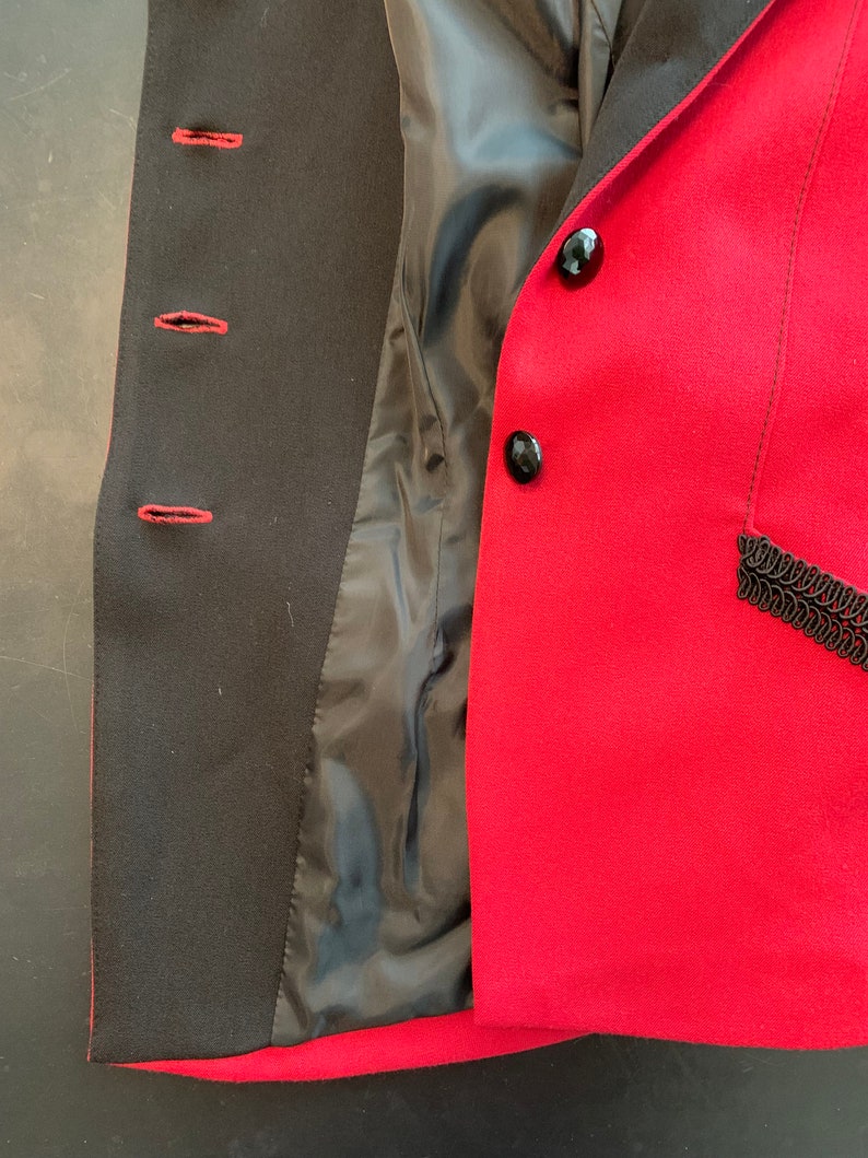 Puede incluir: Una chaqueta roja con botones negros y ribete negro. La chaqueta est&aacute; desabrochada y el forro es visible.