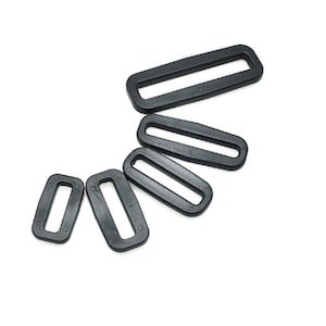 Puede incluir: Cinco hebillas deslizantes de plástico negro de diferentes tamaños. Las hebillas están dispuestas en forma de semicírculo.
