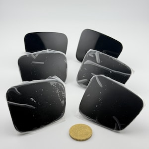 Peut inclure: Six objets noirs rectangulaires, possiblement des pièces automobiles, sont présentés sur une surface blanche. Chaque objet est emballé individuellement dans du plastique transparent. Une pièce d'or est placée à côté pour comparaison.