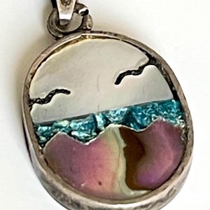 May include: A silver pendant with a seashell inlay. The seashell is a multi-colored iridescent design with a blue and white top and a pink and brown bottom. The pendant is oval shaped and has a silver bail.