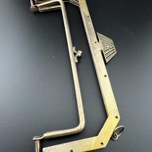 Könnte beinhalten: Ein antikes Werkzeug aus silberfarbenem Metall mit einem einzigartigen geometrischen Design. Das Werkzeug verfügt über eine Reihe von Gelenkarmen und ein dekoratives, fächerförmiges Element. Das Werkzeug hat einen Ring am Ende und scheint ein Spezialinstrument zu sein.