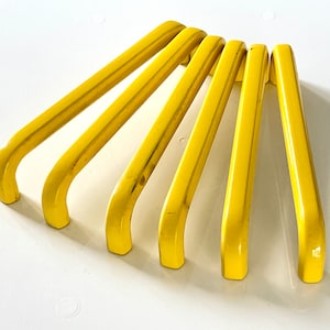 Könnte beinhalten: Sieben gelbe Kunststoff-Schranktürgriffe mit abgerundeter rechteckiger Form.