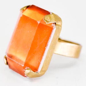 May include: A gold ring with a large, rectangular, orange gemstone.