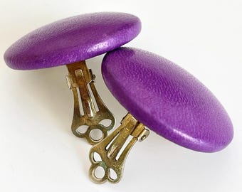 May include: A pair of purple clip-on earrings with a textured finish. The earrings are round and have a gold metal clip.