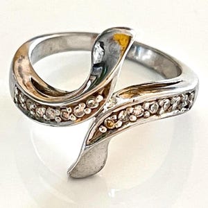 May include: A silver ring with a wave-like design and small clear stones set along the band.