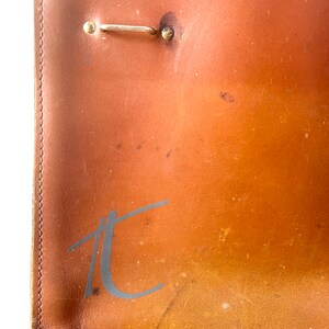 May include: Close-up of a brown leather chair with a metal hook and the letter "T" embossed on the back.