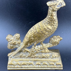 Könnte beinhalten: Eine detaillierte Messing-Skulptur eines Fasans, der auf einem Ast sitzt, mit komplizierten Federdetails. Der Vogel ist auf einem rechteckigen Sockel mit dekorativem Rand montiert. Die Skulptur hat ein Vintage- und antikes Aussehen.