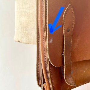 May include: A brown leather satchel bag with a flap closure and a strap. The bag has a worn look and is made of thick leather.