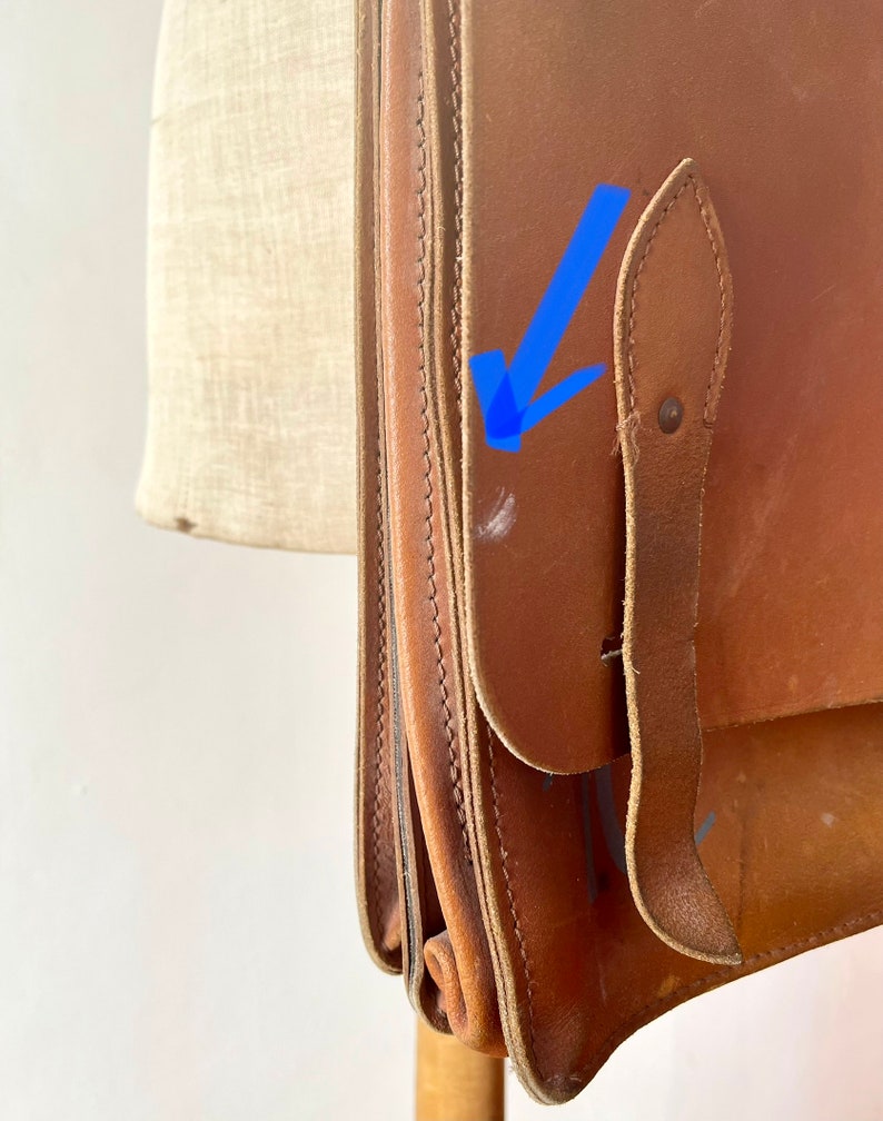 May include: A brown leather satchel bag with a flap closure and a strap. The bag has a worn look and is made of thick leather.