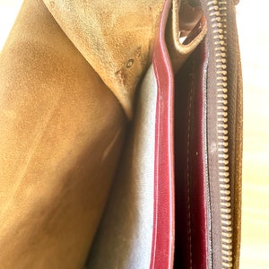 May include: The inside of a brown leather bag with a zipper closure. The bag is lined with a red fabric and has a brown suede lining.