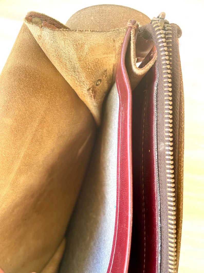 May include: The inside of a brown leather bag with a zipper closure. The bag is lined with a red fabric and has a brown suede lining.
