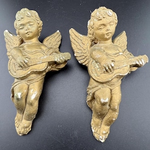 Puede incluir: Dos figuras antiguas de querubines dorados, cada una tocando una guitarra. Los querubines tienen los ojos cerrados y alas detalladas. Las figuras tienen un acabado envejecido, lo que añade encanto vintage. Ideal para la decoración del hogar.