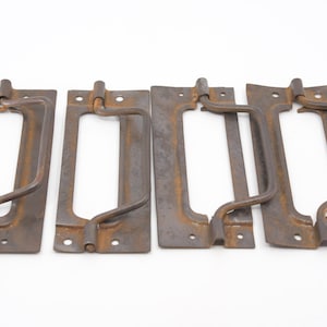 May include: Four rusty metal drawer pulls with a rectangular shape and a curved handle. The pulls have a distressed, vintage look.