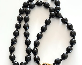 May include: A black beaded necklace with a gold clasp. The beads are faceted and have a shiny finish.