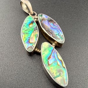 May include: A silver pendant with three iridescent abalone shell pieces in a teardrop shape. The pendant is a statement piece with a unique design.