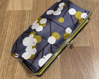 May include: A rectangular clutch with a silver clasp. The clutch features a floral pattern with white and yellow flowers on a dark blue background. The interior is yellow.